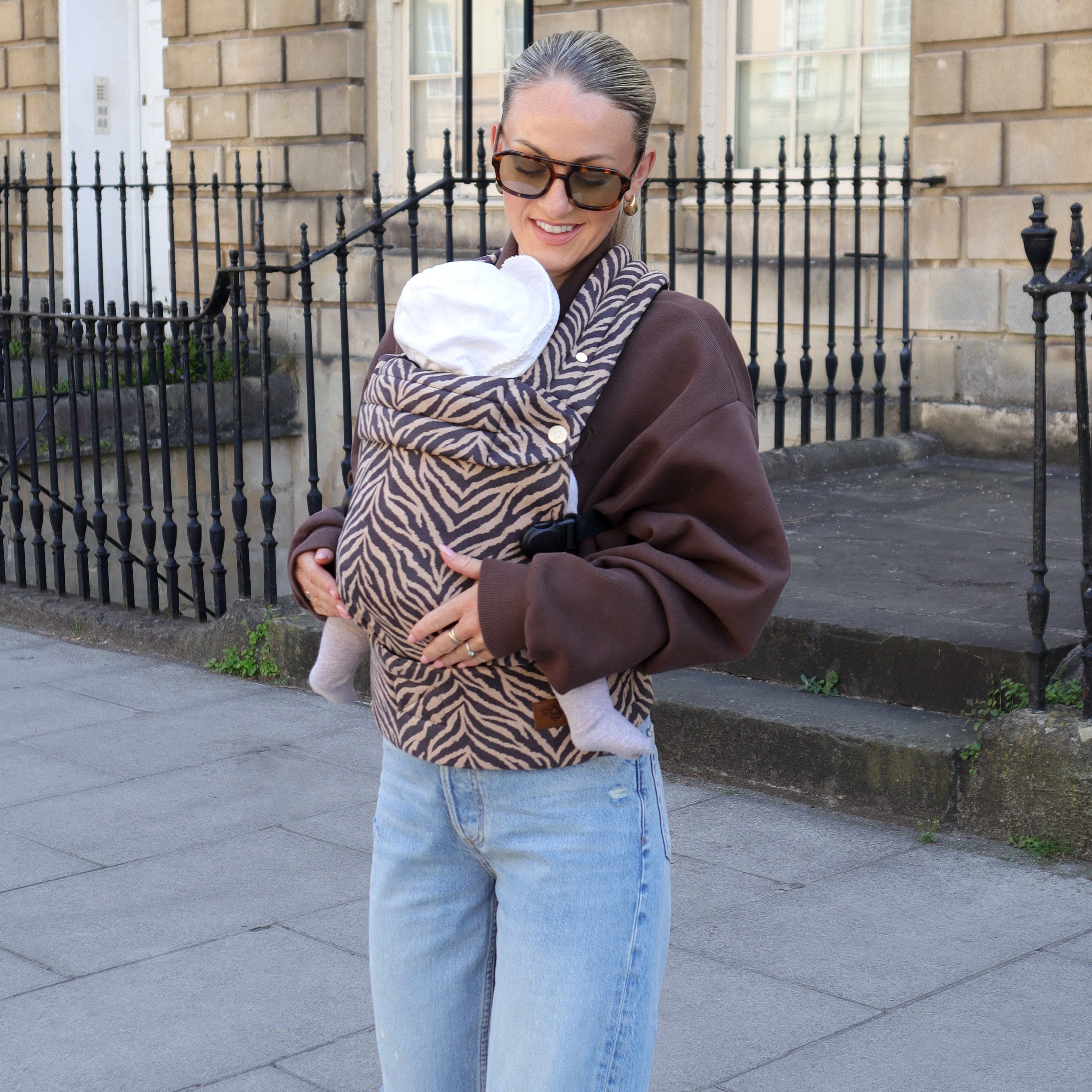 Woman carrying a baby in a sling on a city street.