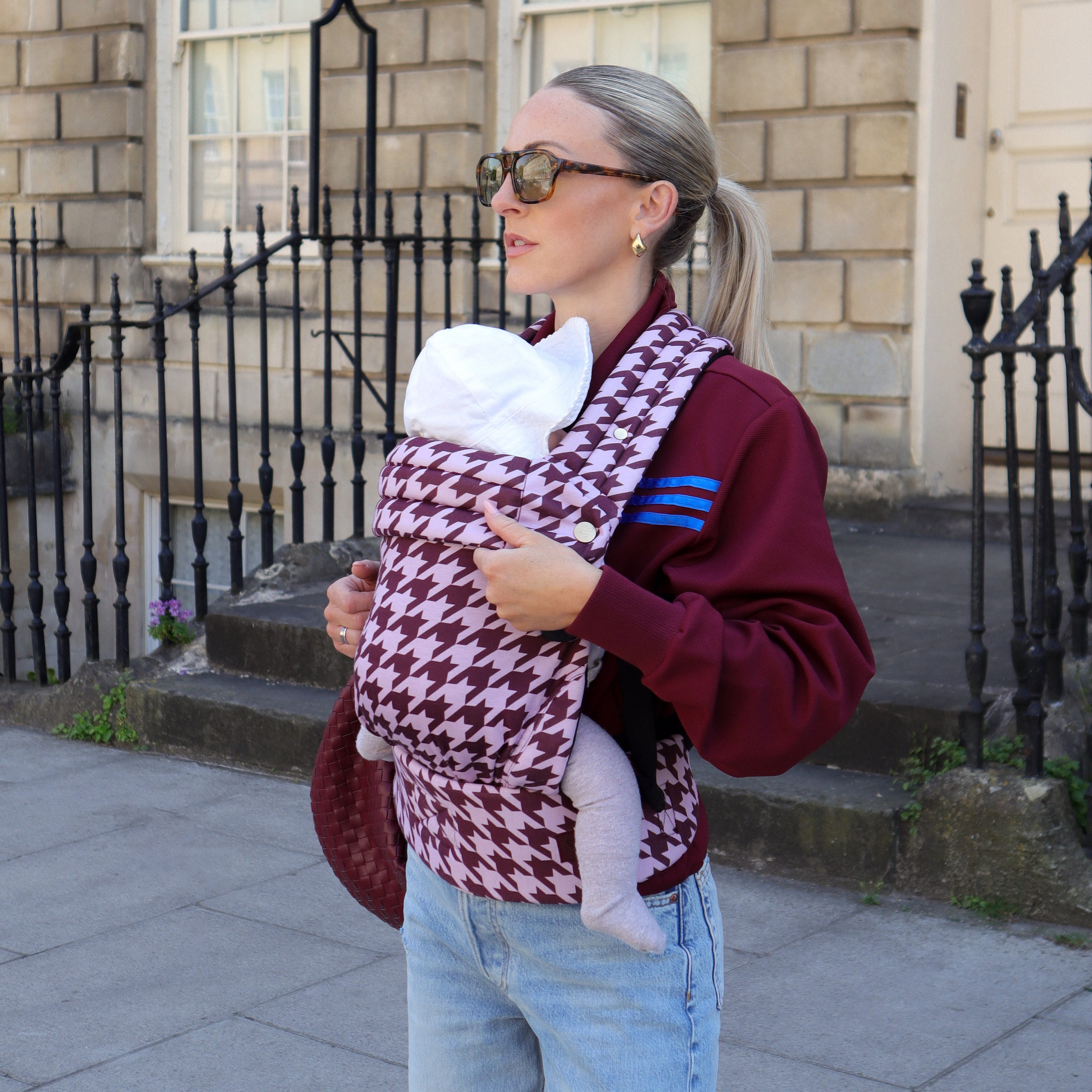 Woman carrying a baby in a houndstooth-patterned carrier outdoors.