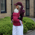 Woman carrying a baby in a pink baby carrier outdoors.