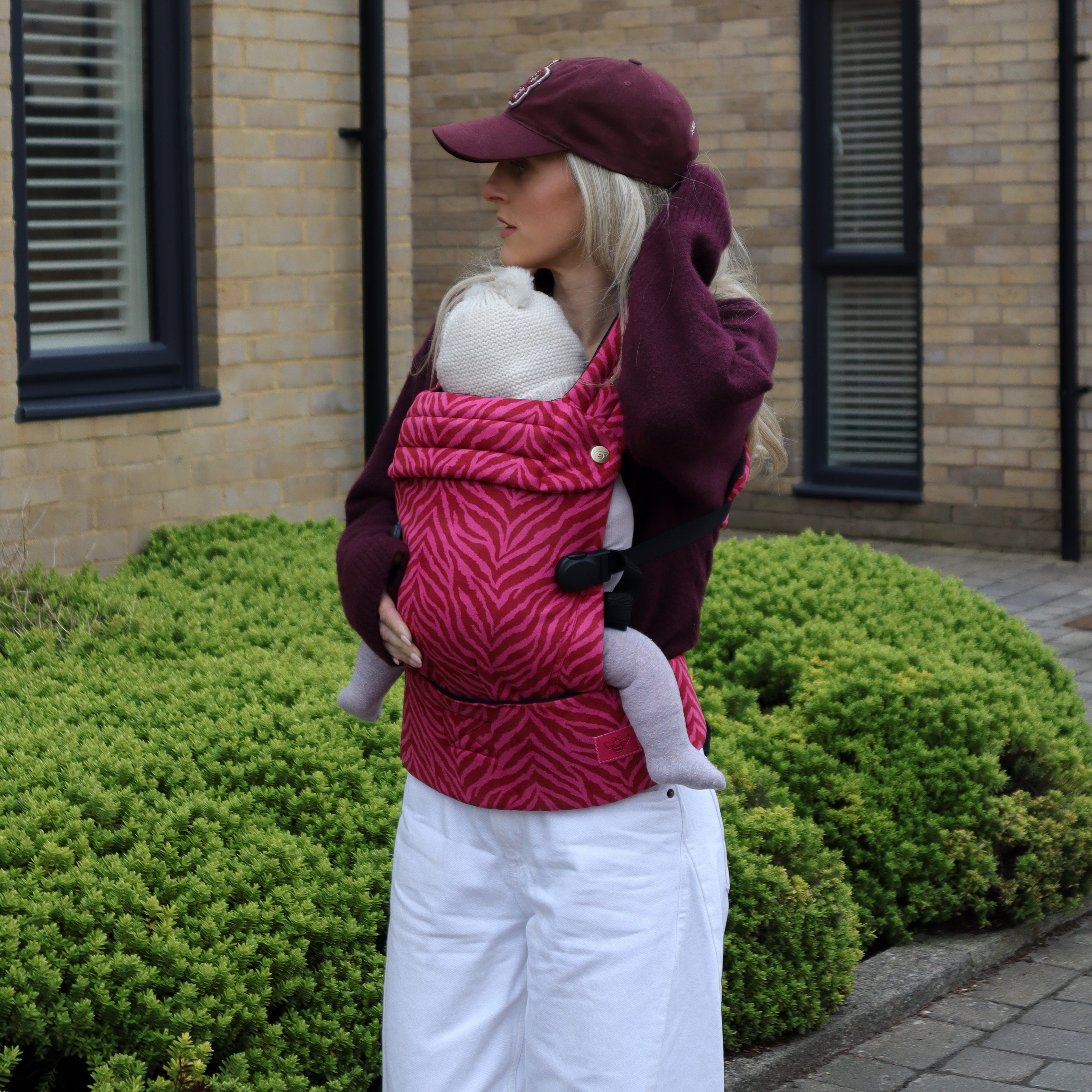 Woman carrying a baby in a pink baby carrier outdoors.