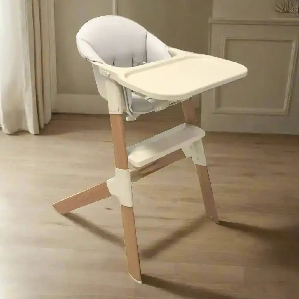 Baby high chair with white tray and beige legs on a wooden floor.