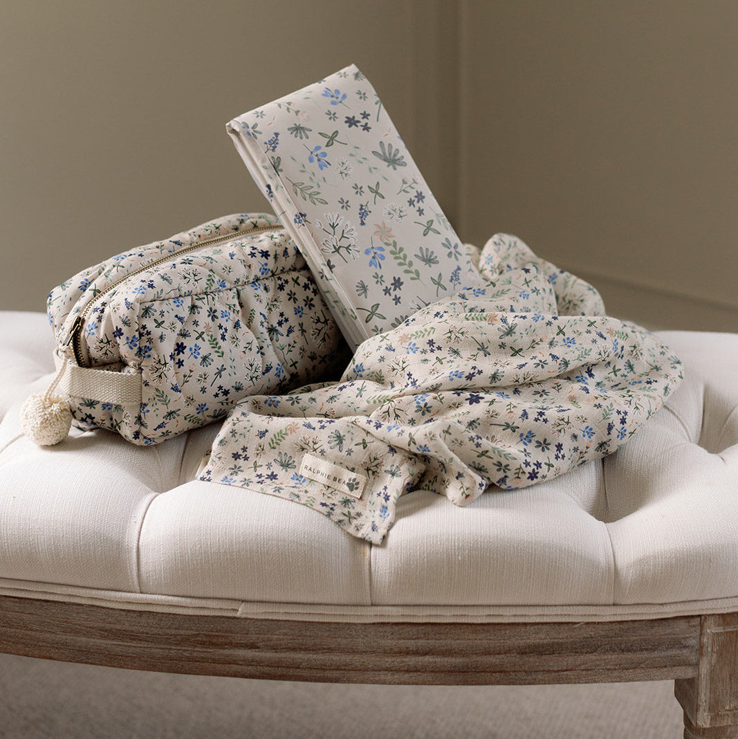 Floral-patterned pillows and blanket on a beige cushioned bench against a plain wall.