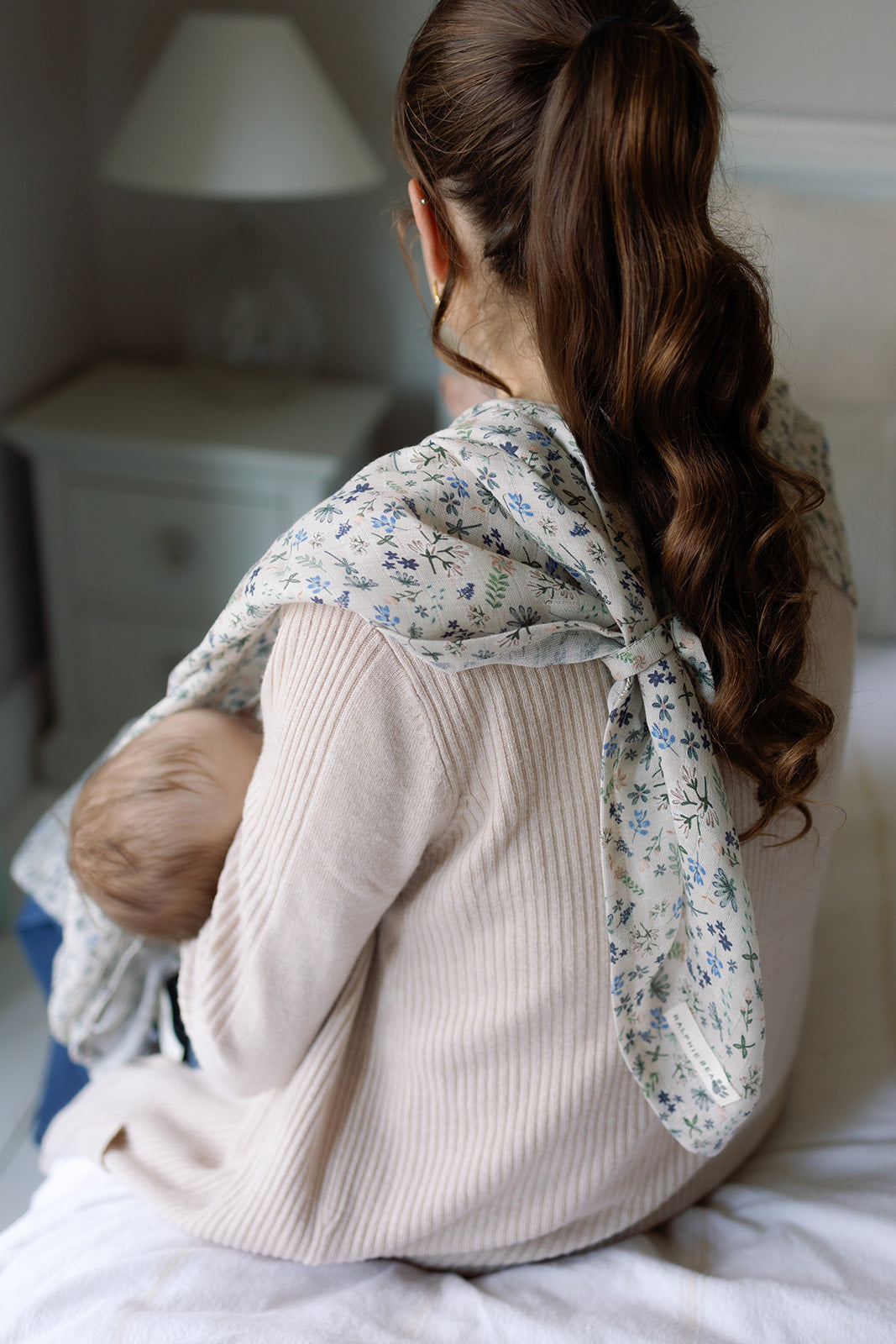 Woman holding a baby wrapped in a floral blanket in a bedroom setting