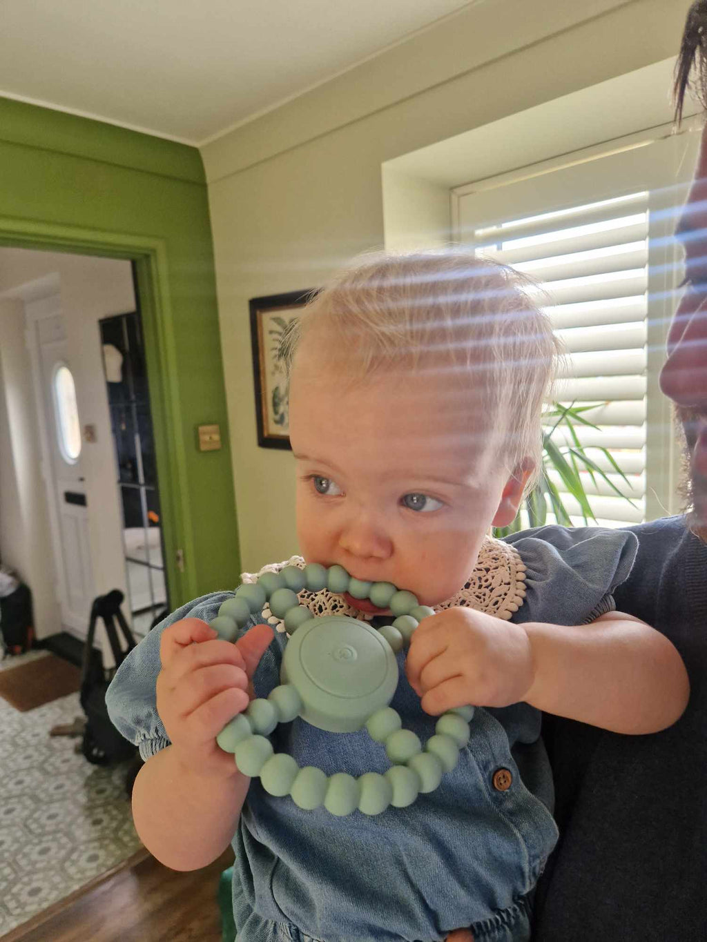 Baby holding a green teething ring with a person partially visible