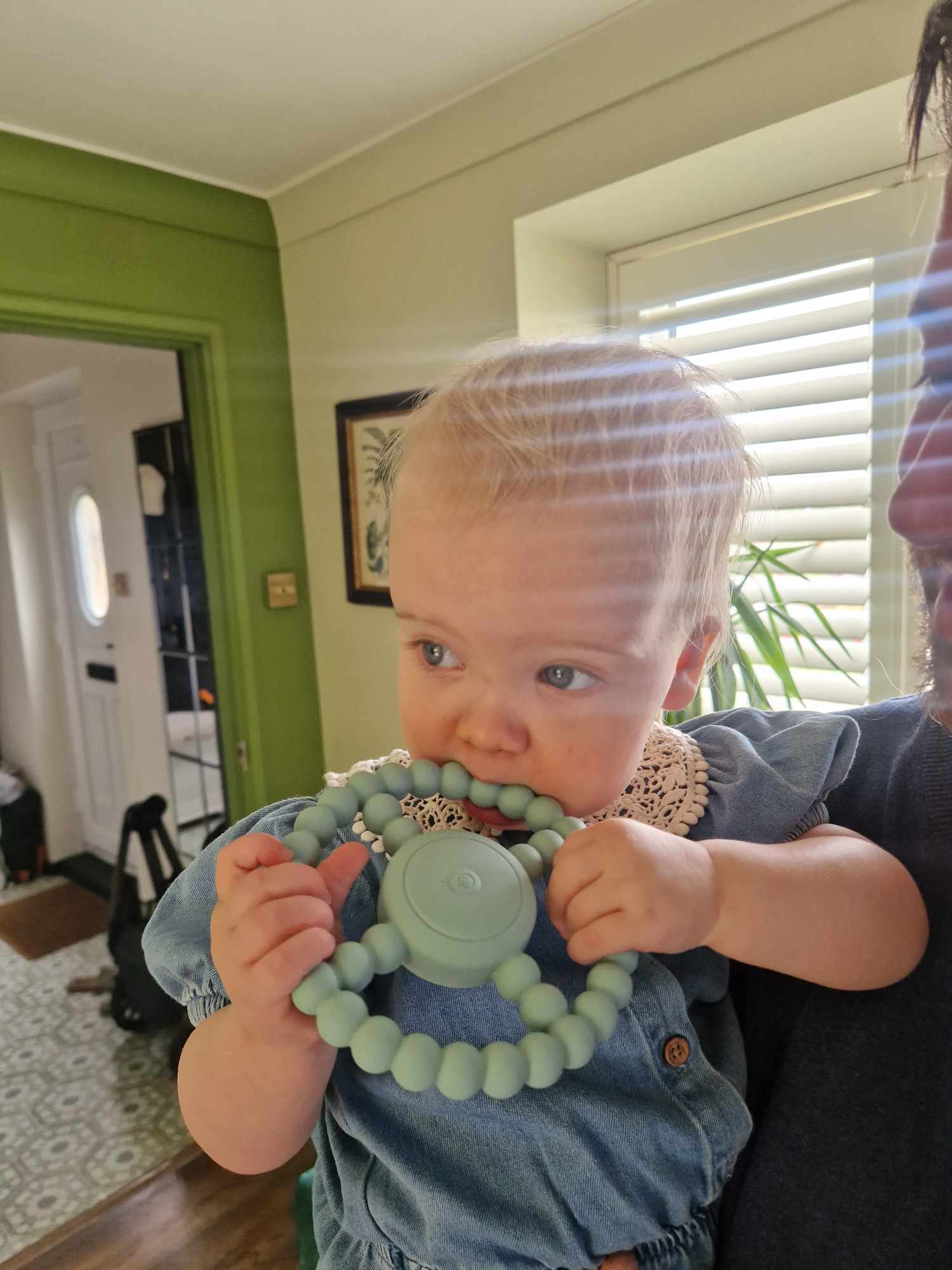 Baby holding a green teething ring with a person partially visible