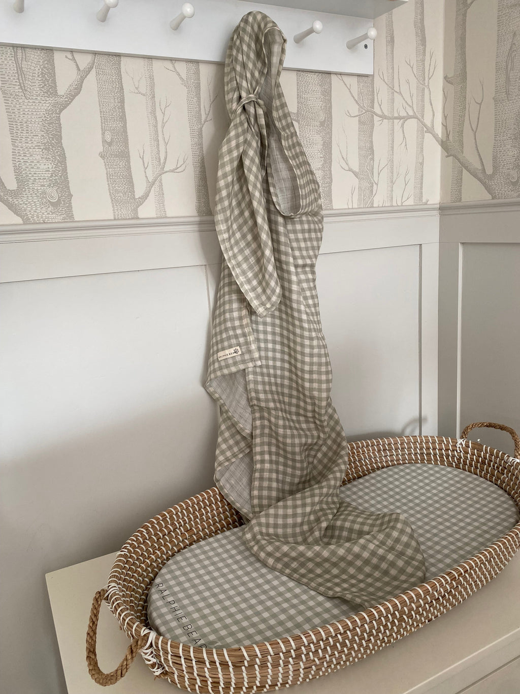 Wicker crib with checkered blanket against a wall with tree pattern