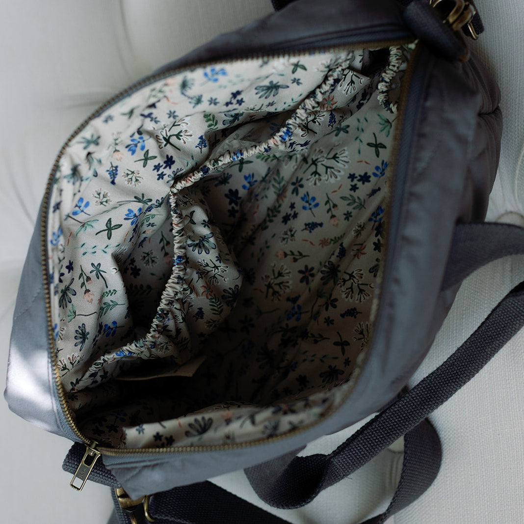 Floral-patterned lining of a gray backpack on a white cushioned surface