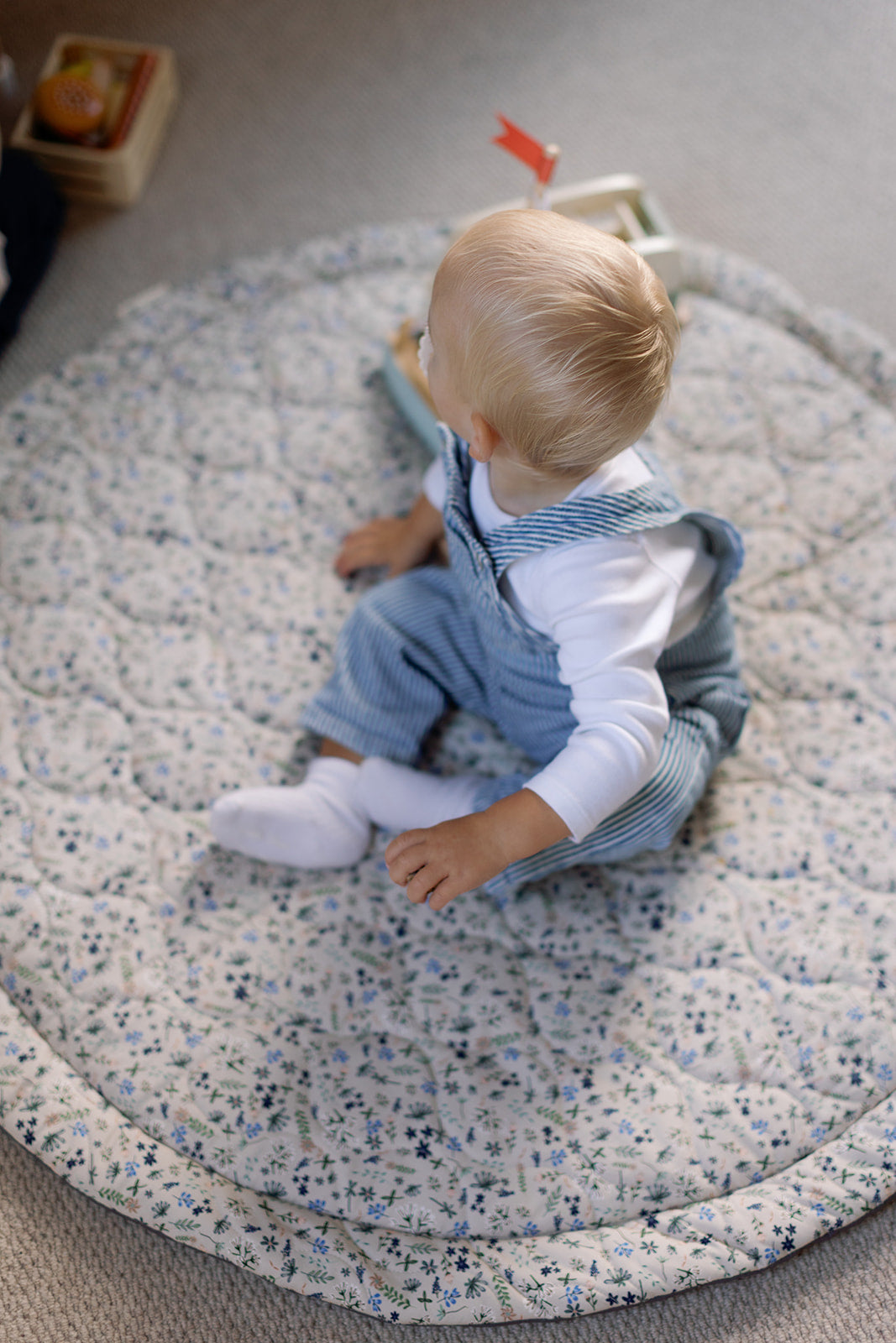Baby sitting on a textured play mat with a toy in the background