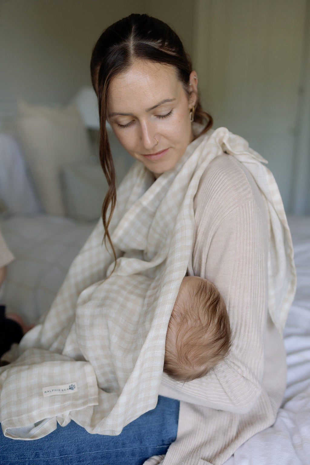 Woman holding a baby wrapped in a light-colored blanket indoors.