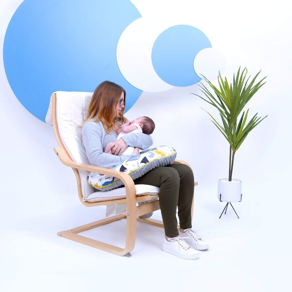 Woman breastfeeding a baby in a chair with a blue and white abstract design in the background
