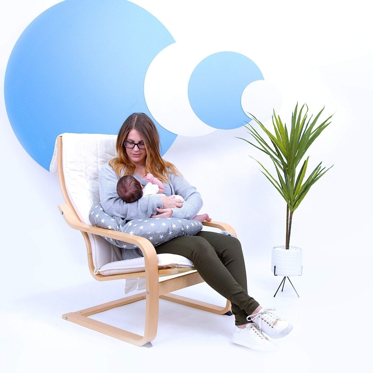 Woman breastfeeding a baby in a chair with a white background and blue abstract shapes.