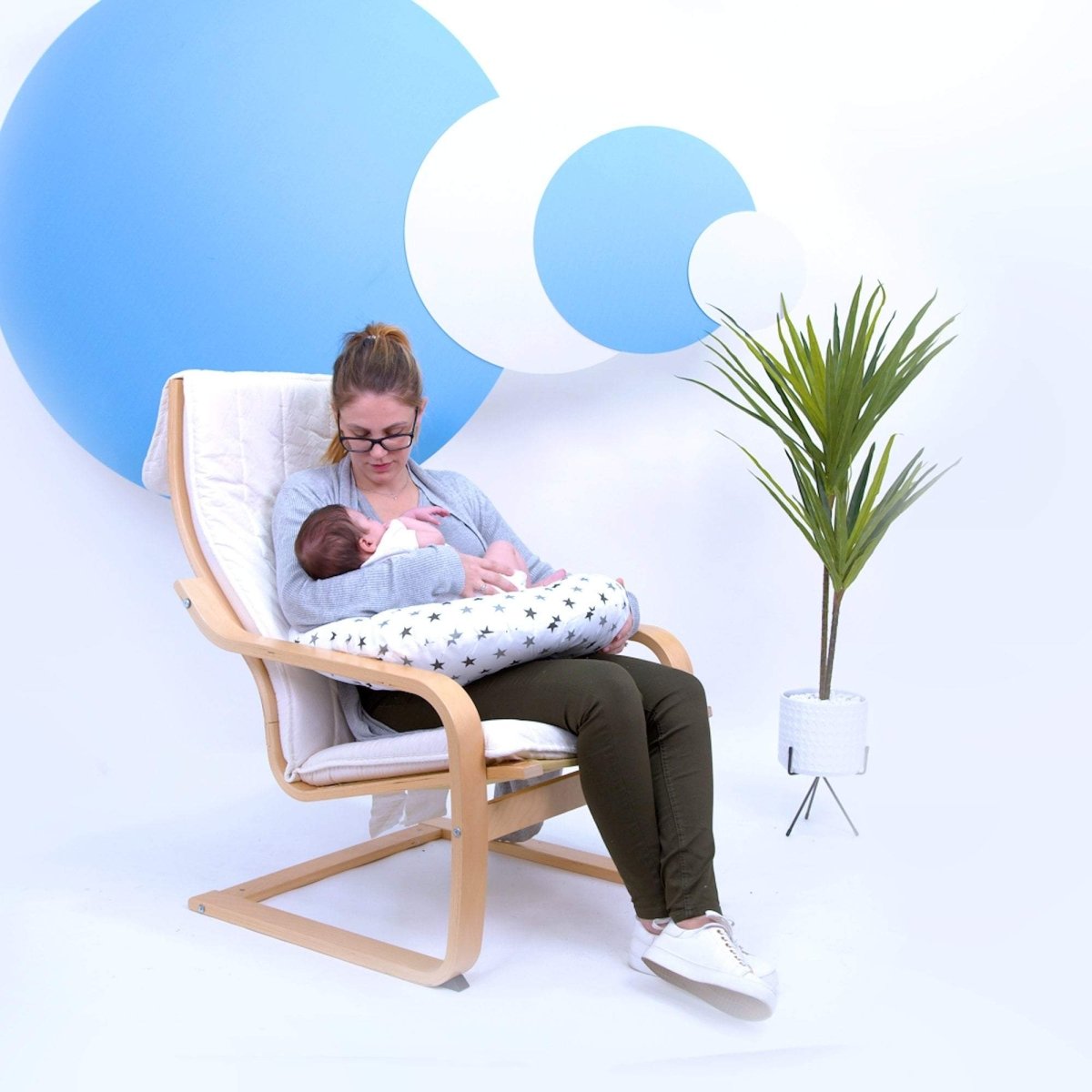 Woman breastfeeding a baby in a chair with a white background and blue abstract shapes.
