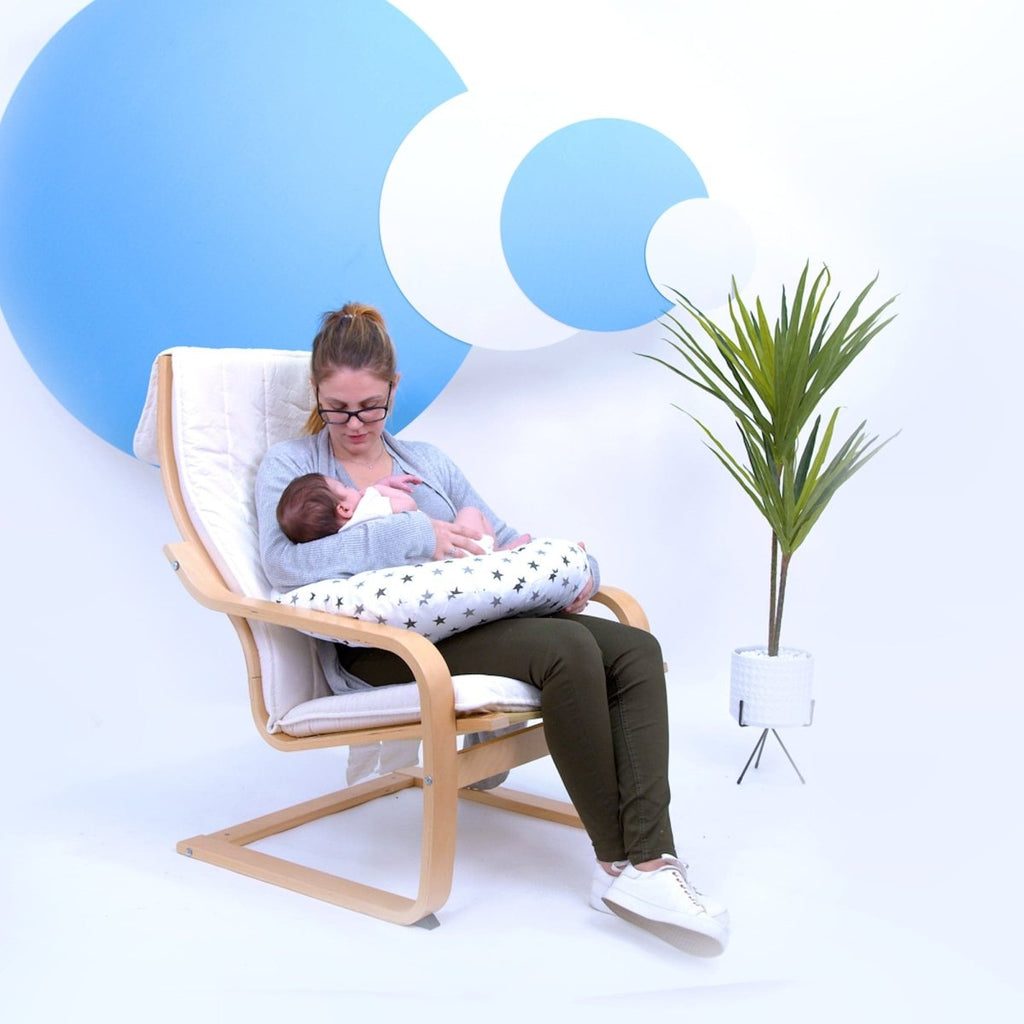 Woman breastfeeding a baby in a chair with a white background and blue abstract shapes.