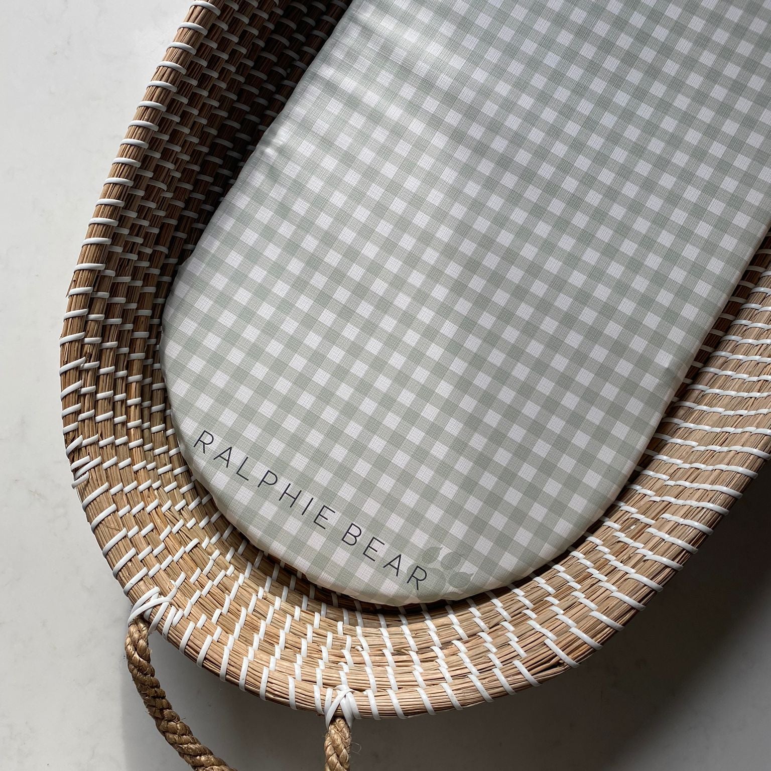 Wicker baby crib with a gray checkered mattress, branded 'Ralphie Bear'.