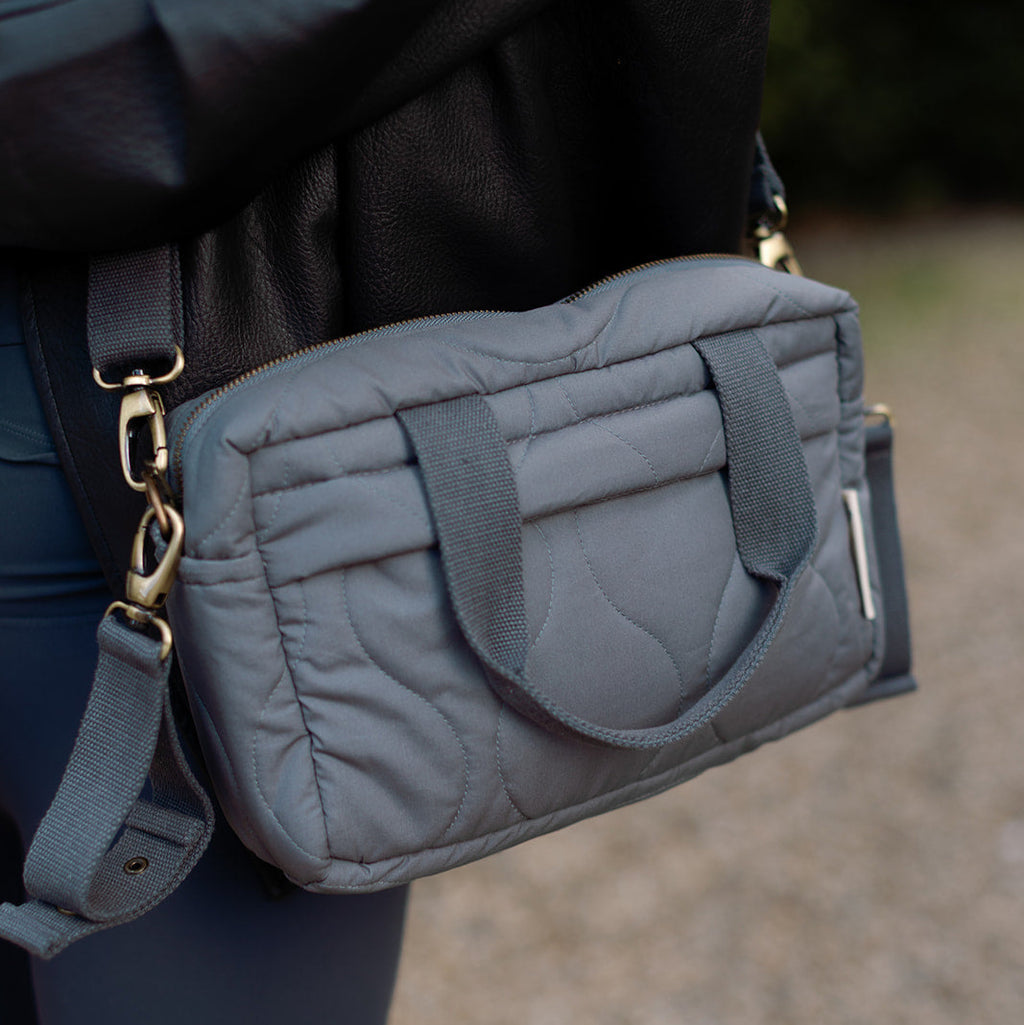 Gray quilted handbag with gold accents held by a person outdoors.