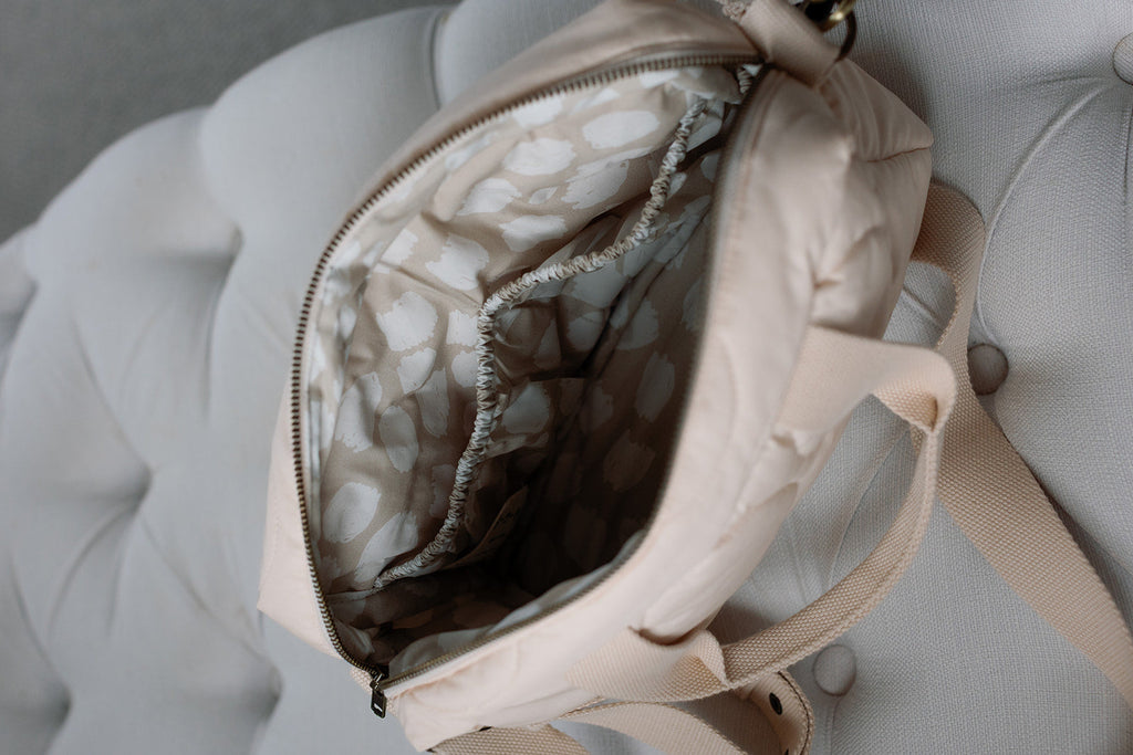 Beige backpack with open front pocket on a light gray cushioned surface