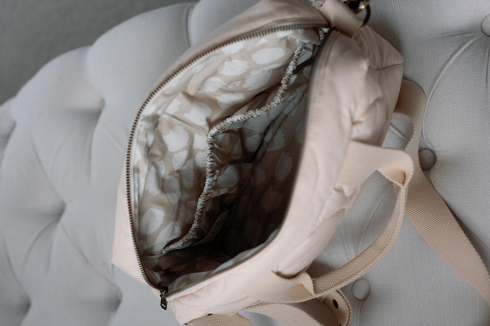 Beige backpack with open front pocket on a light gray cushioned surface