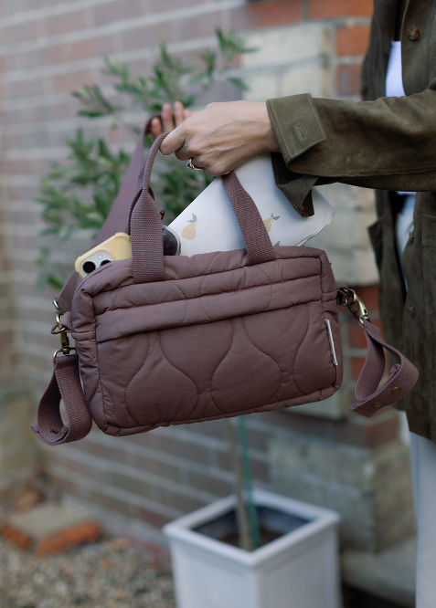 Person holding a brown quilted handbag with a blurred background