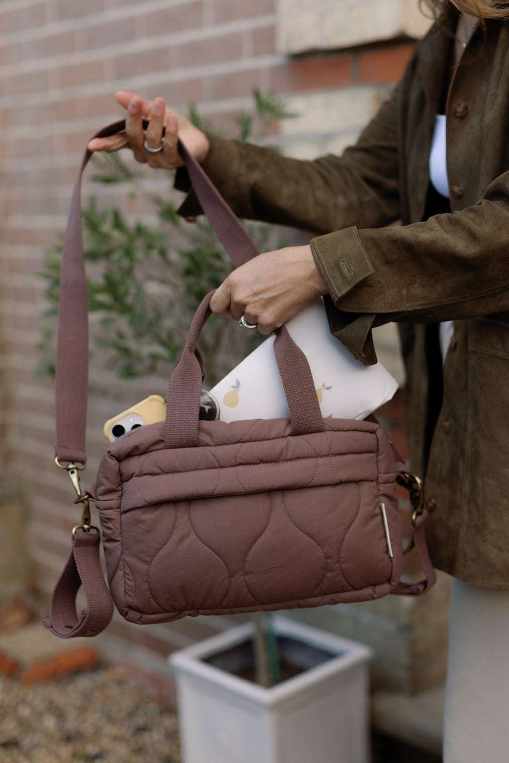 Person holding a brown quilted handbag with a phone case on a blurred background