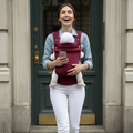 Woman carrying a baby in a sling and using a phone, standing outside a building.