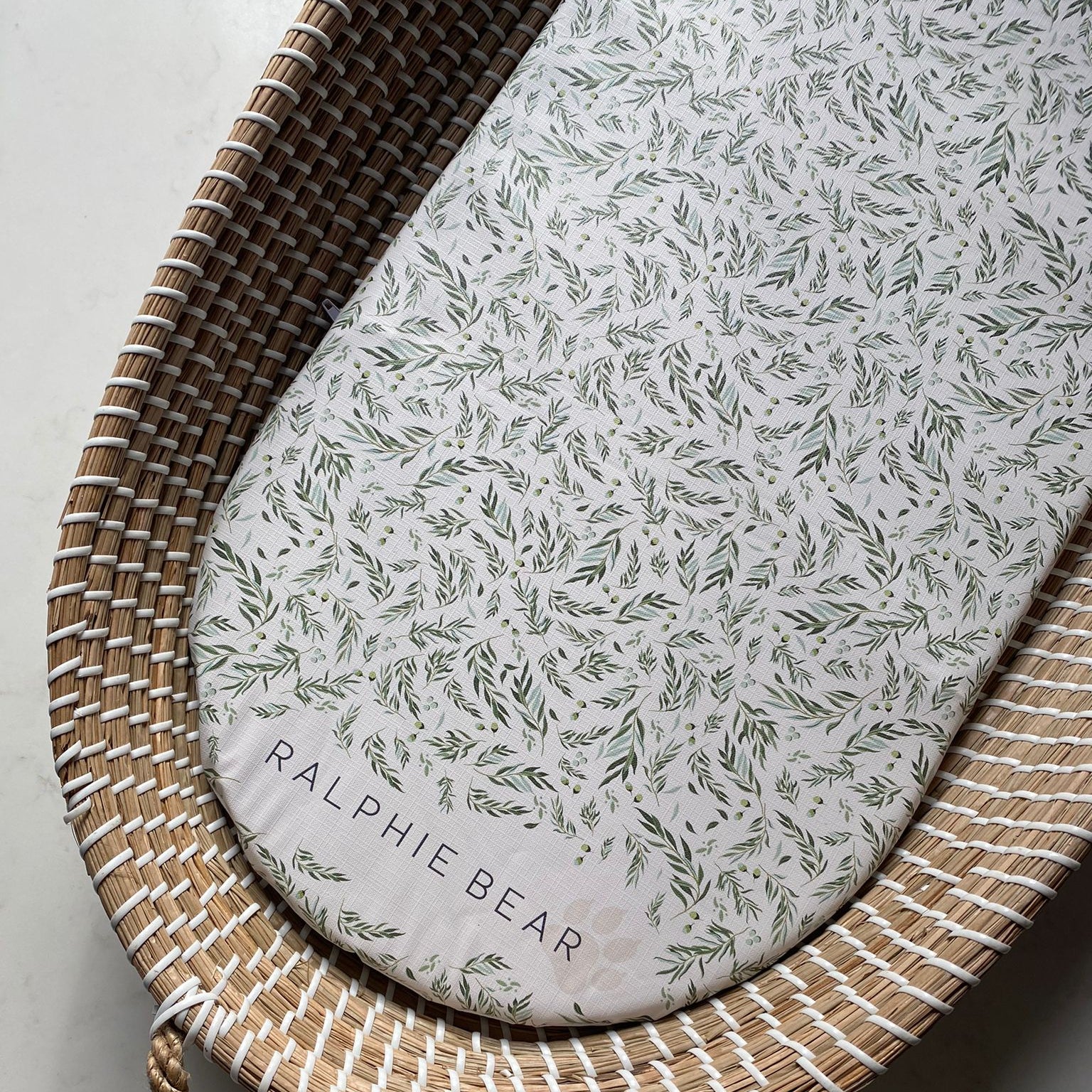 Wicker basket with a floral-patterned cushion labeled 'Ralphie Bear' on a light background