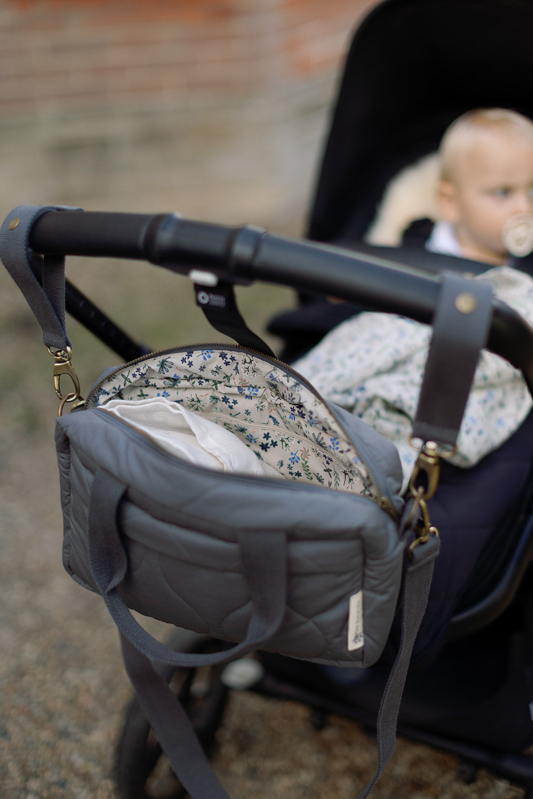 Gray diaper bag attached to a stroller with a blurred background