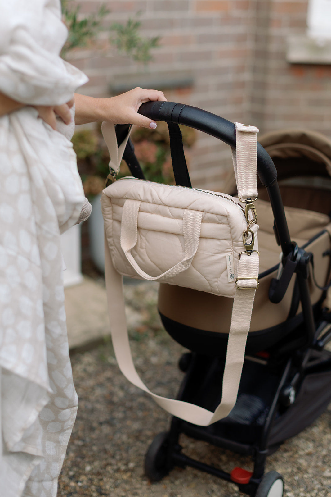 Person holding a beige quilted handbag with a stroller in the background