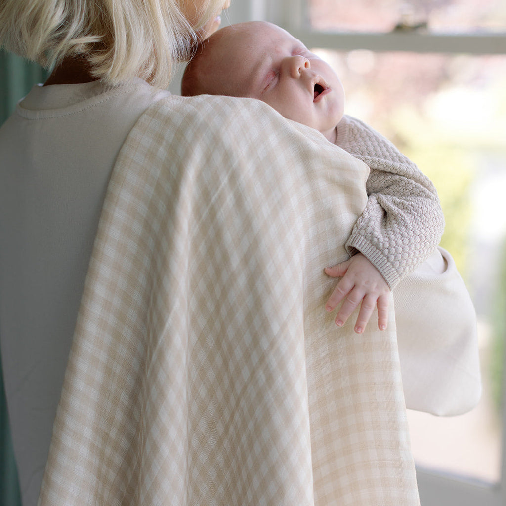 Woman holding a baby wrapped in a textured blanket with a blurred outdoor background