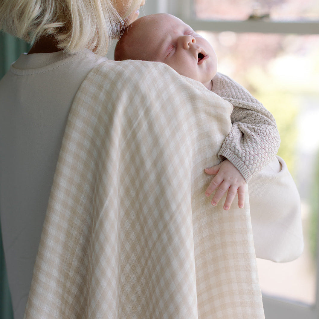 Woman holding a baby wrapped in a textured blanket with a blurred outdoor background