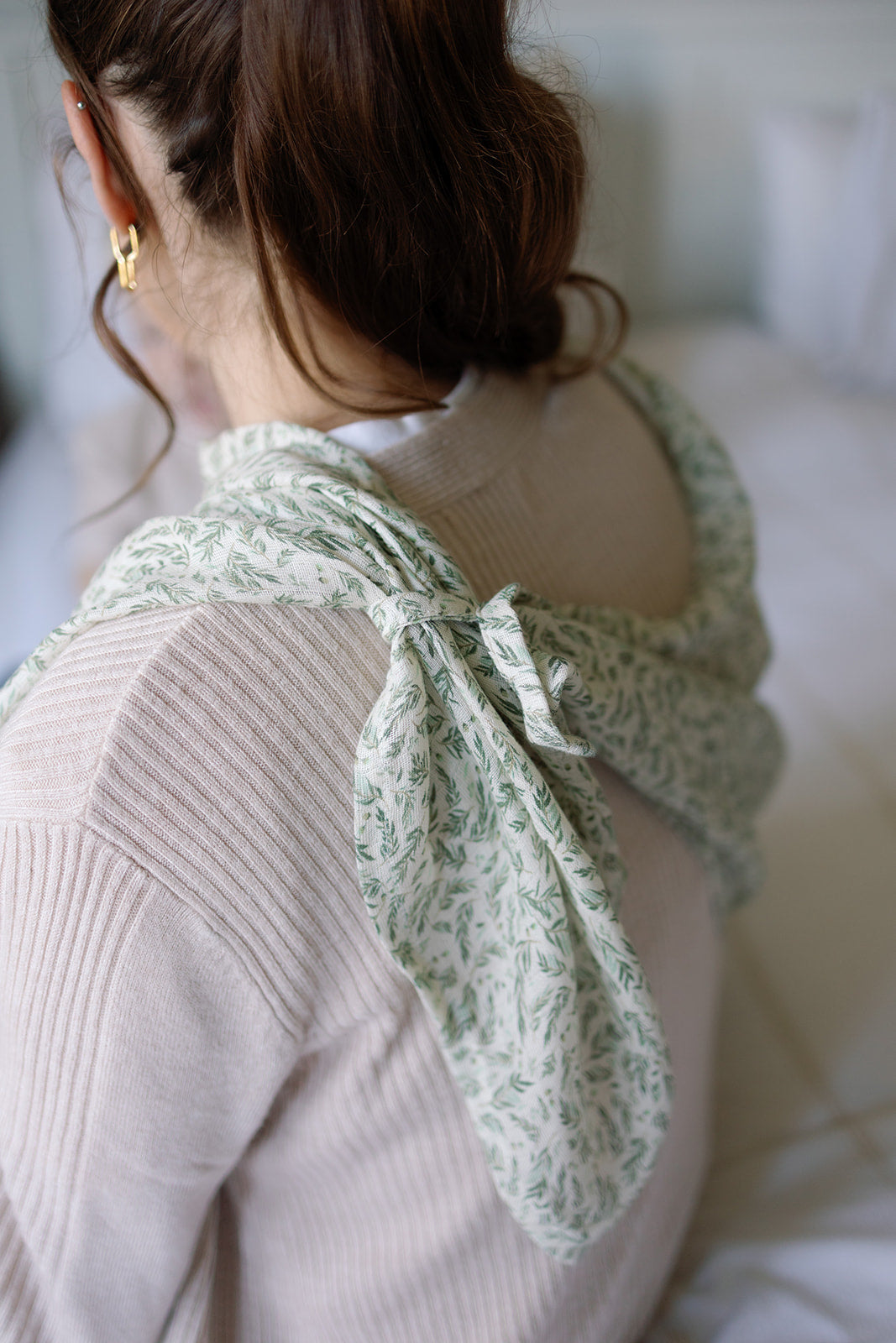 Person wearing a light pink sweater with a green floral scarf draped over their shoulders.