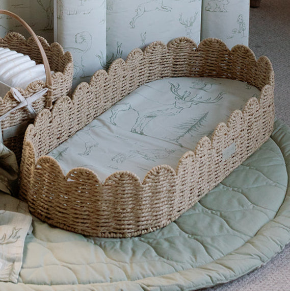 Wicker crib with a soft mattress and decorative elements on a light green blanket.