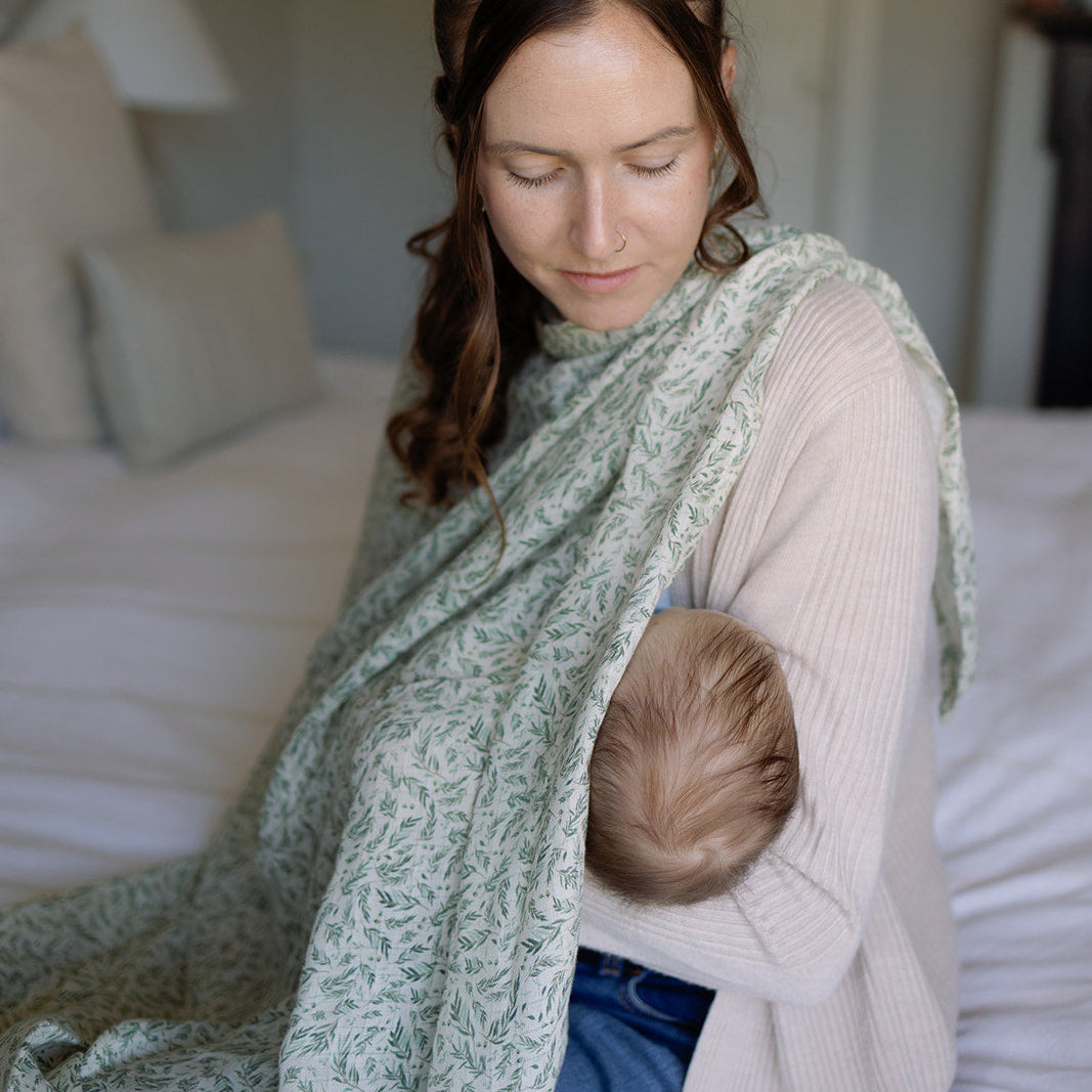 Woman breastfeeding a baby using a green wrap in a bedroom setting.