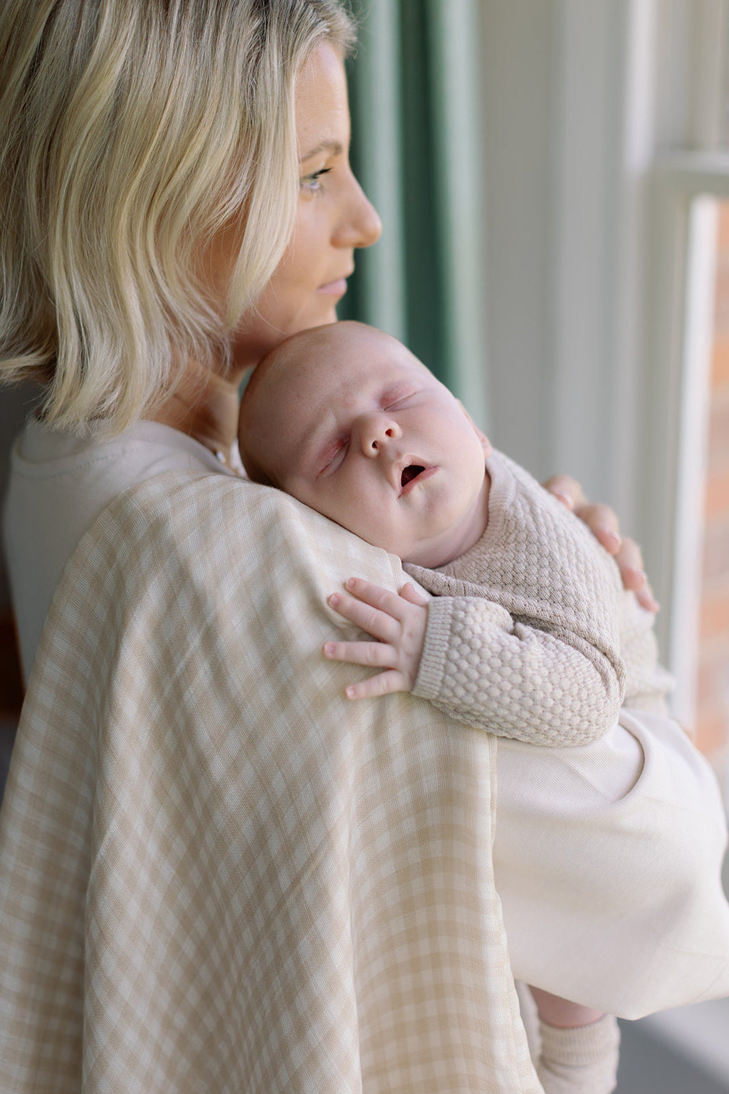 Woman holding a baby wrapped in a beige blanket indoors.