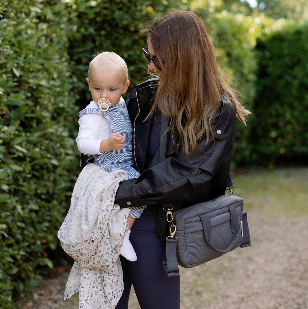 Woman holding a baby outdoors with greenery in the background