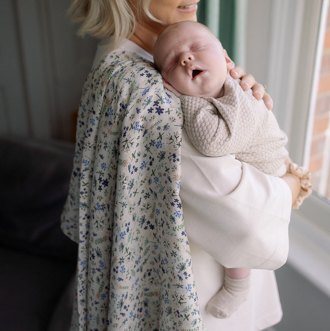 Woman holding a baby in a room with a window and green curtain.