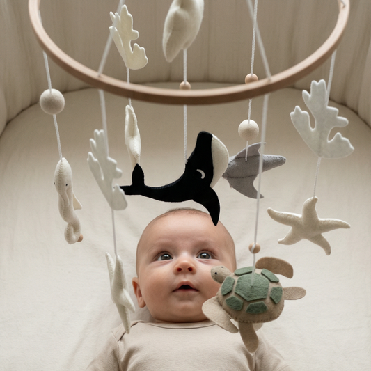 Baby lying on a white blanket with a mobile above, featuring sea-themed toys.