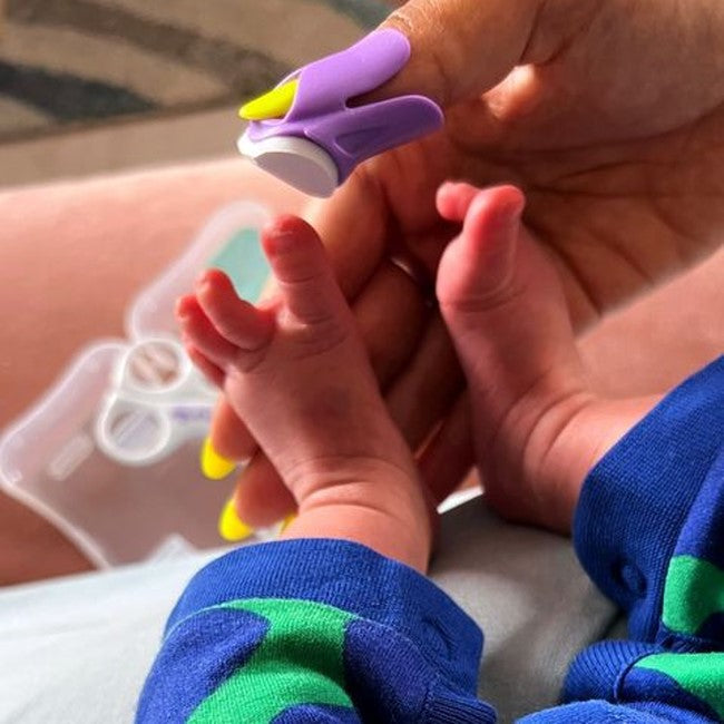 Baby's feet being held by an adult hand with a purple nail clipper in the background.